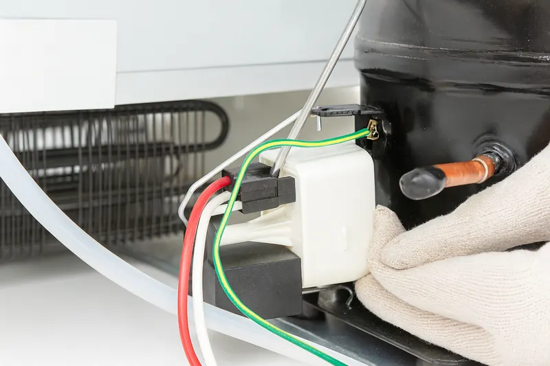 Side of a refrigerator compressor with the start relay and overload protector plugged onto its terminals