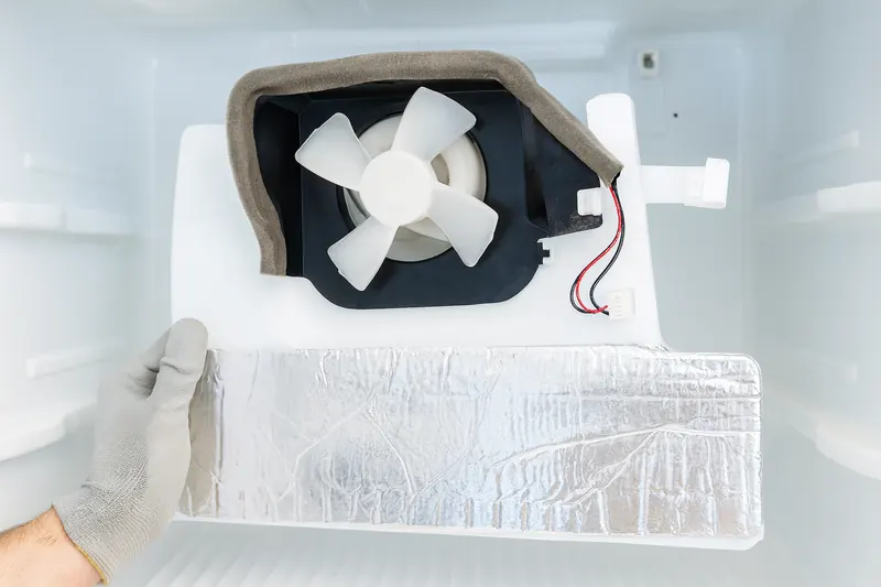 Freezer with the rear evaporator cover removed, showing the evaporator fan and the top of a lightly frosted evaporator coil