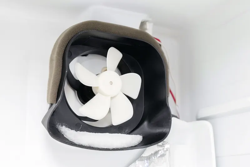 Evaporator fan behind the freezer panel with a ridge of ice built up against the fan blade