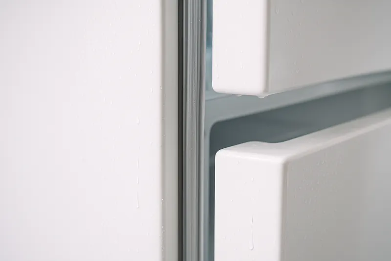 Water droplets condensing along a refrigerator door gasket and the cabinet face